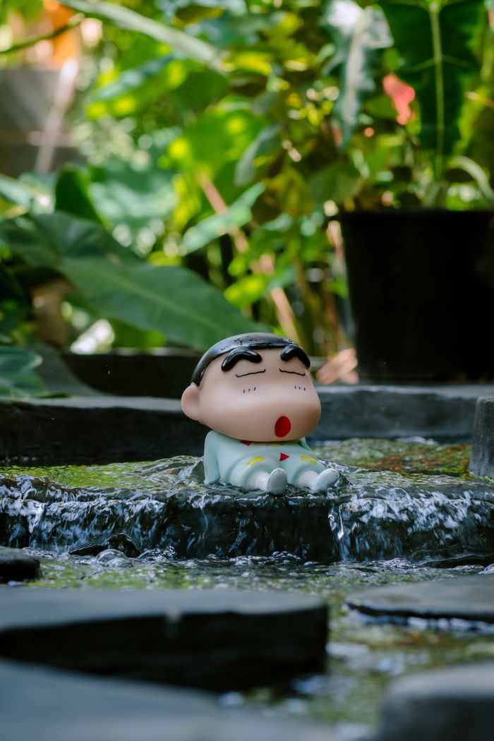 Toy character sitting in a small outdoor stream surrounded by lush greenery.